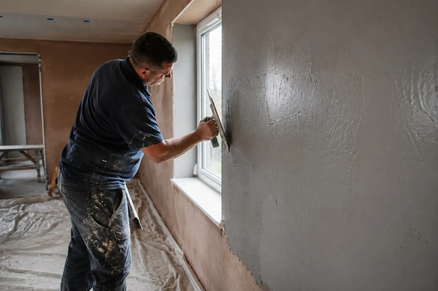 A plasterer skimming a freshly insulated wall around a window reveal in an Irish home